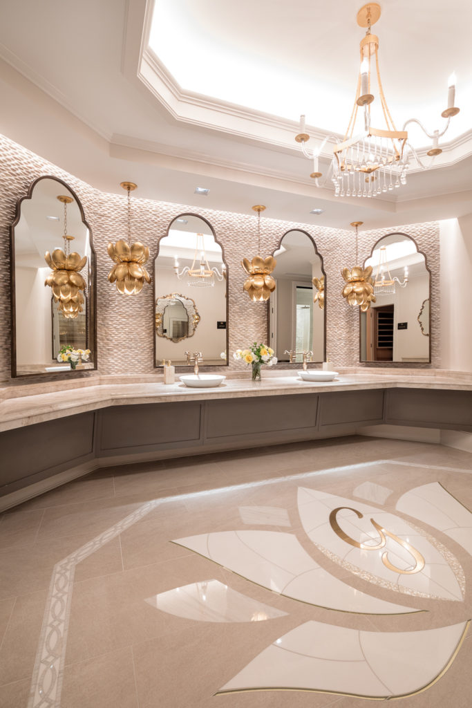 An opulent bathroom with large-format beige floor tiles and a stunning custom waterjet-cut lotus flower tile mosaic with a gold monogram center.